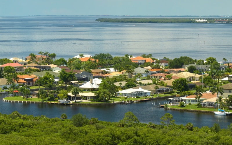 Aerial view of residential suburbs with private homes located near wildlife wetlands with green vegetation on sea shore. Living close to nature concept.