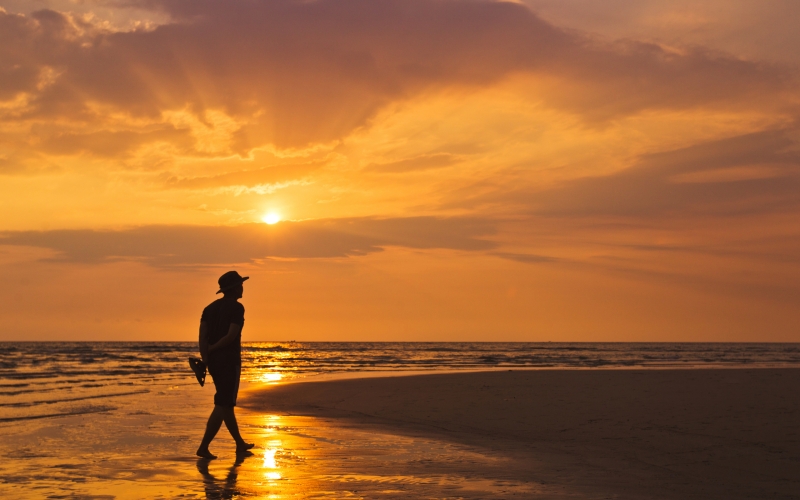 Man walking along the beach at sunset