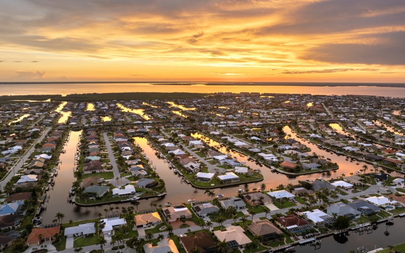 Rich Florida waterfront neighborhood at sundown. Expensive suburban mansions surrounded by palm trees under warm sunset sky